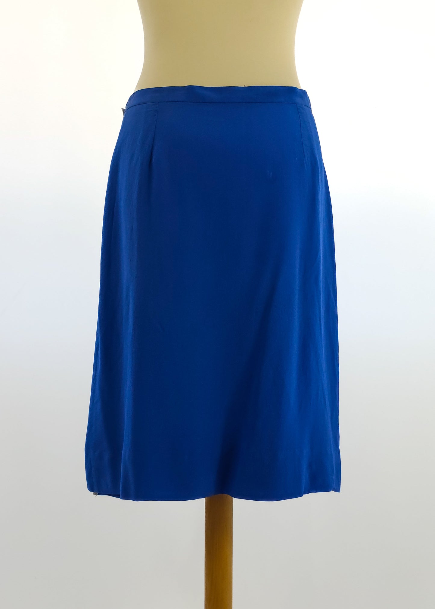 A mannequin displays a knee-length royal blue skirt with a subtle A-line design against a neutral background. The skirt has a simple waistband and smooth fabric texture.