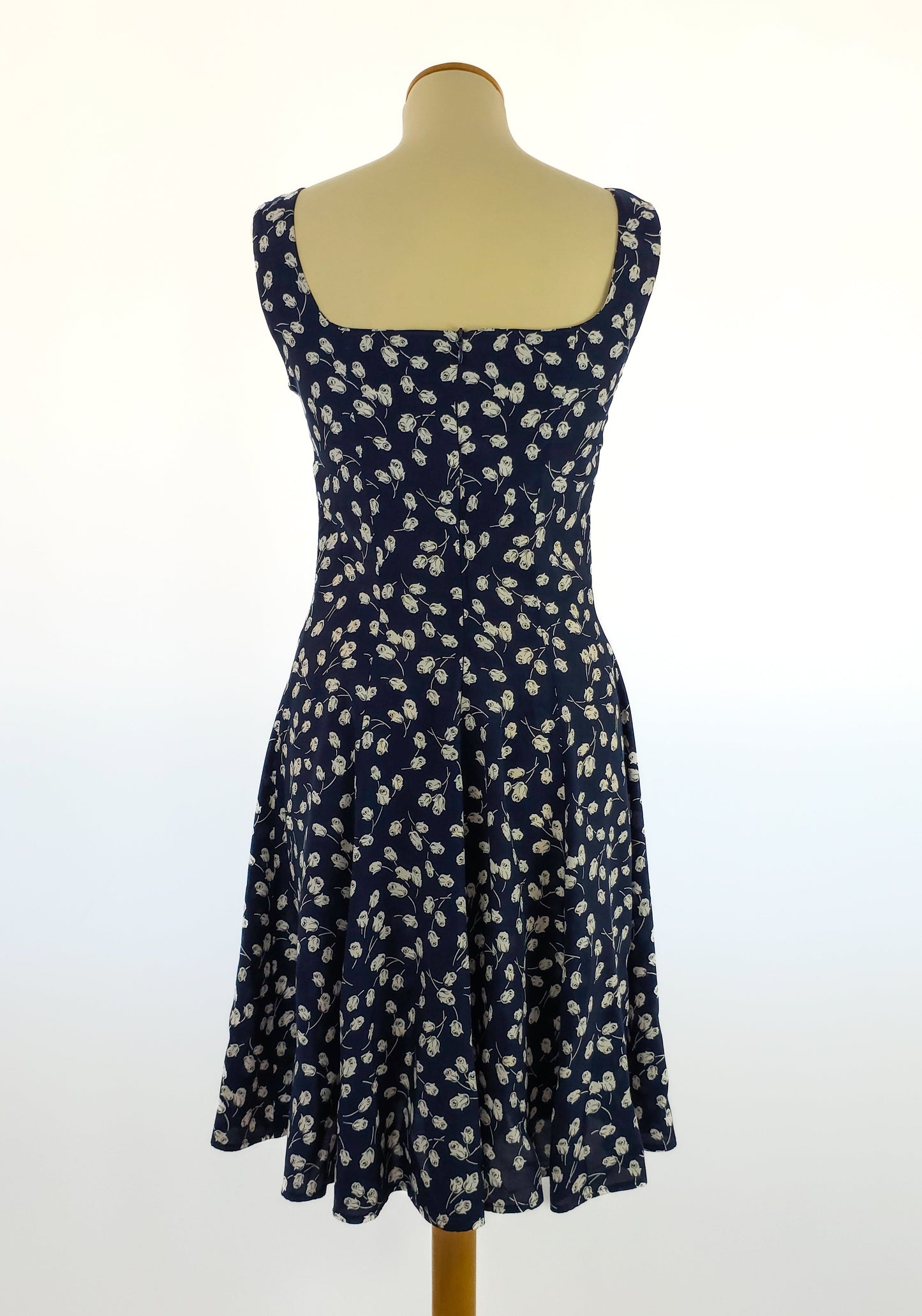 Back view of a navy blue sleeveless dress with a white floral pattern and a flared skirt, displayed on a mannequin against a plain background.