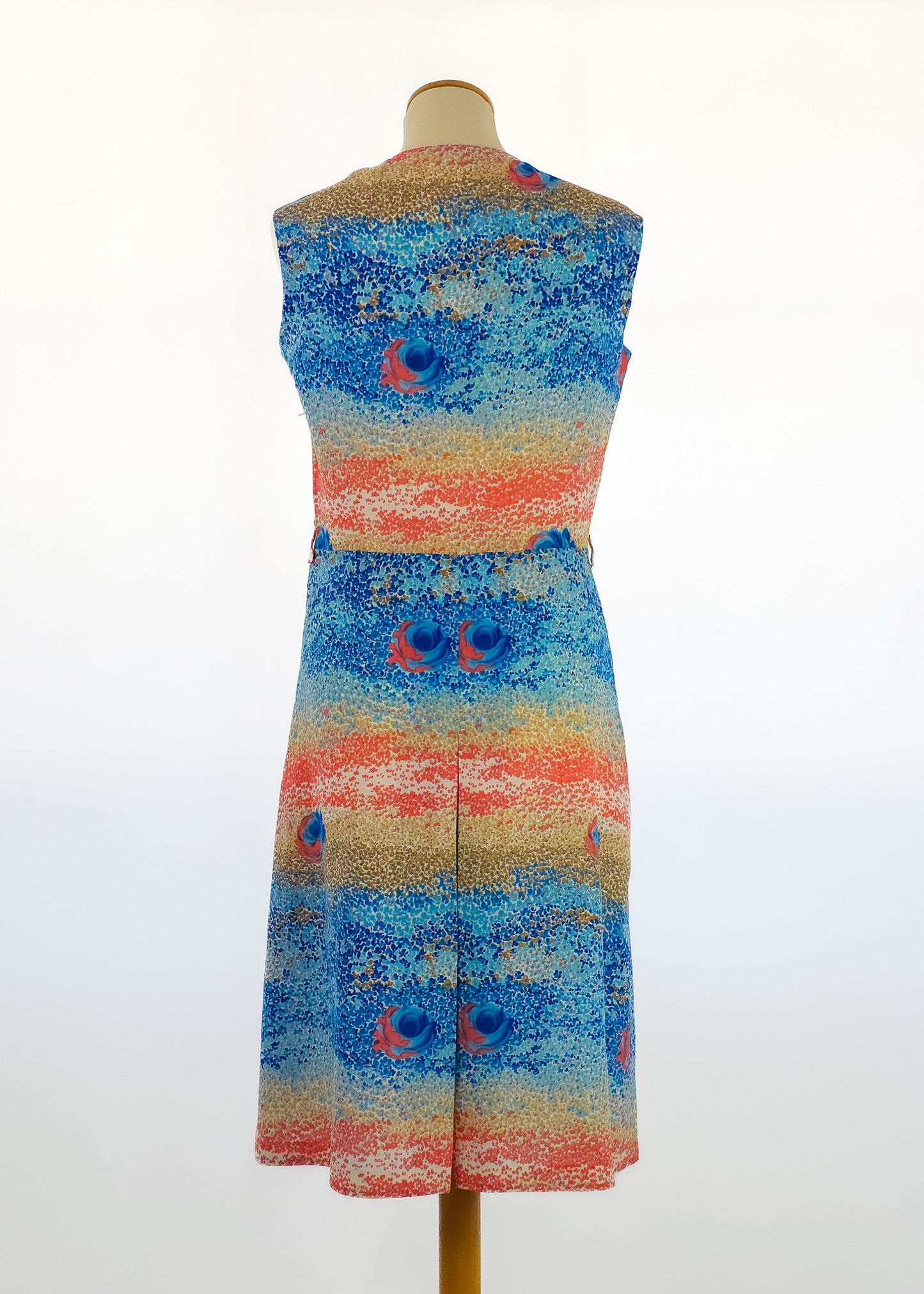 Sleeveless multicolored dress with a speckled pattern and abstract floral motifs on a mannequin. The dress features blue and coral hues.