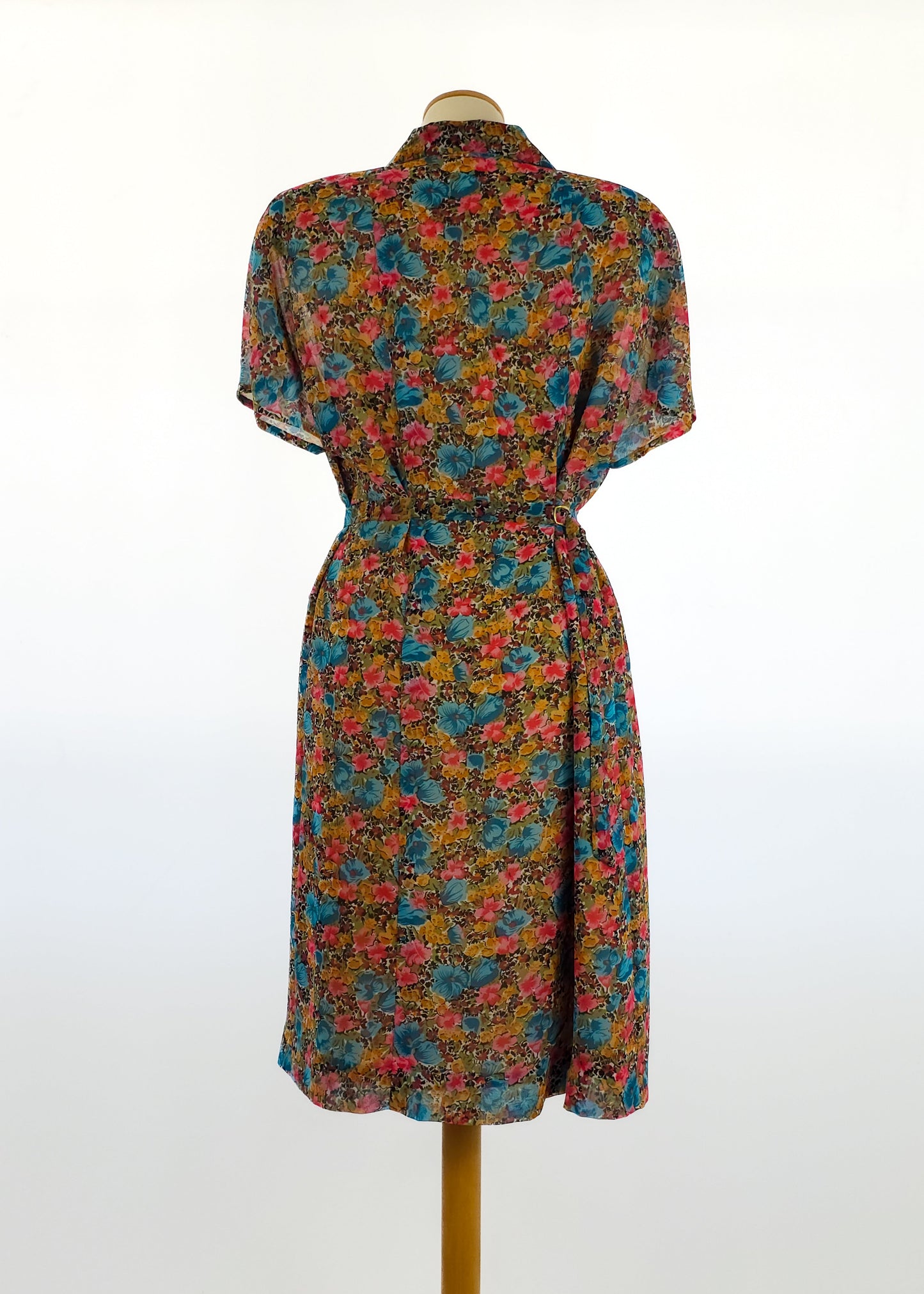 A colorful vintage dress featuring a floral print, short sleeves, and a cinched waist, displayed on a mannequin against a plain white background.