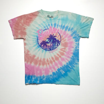 A tie-dye T-shirt featuring a spiral pattern and Barbie logo print in pastel colors of blue, pink, and purple, displayed on a plain white background. The shirt is short-sleeved.