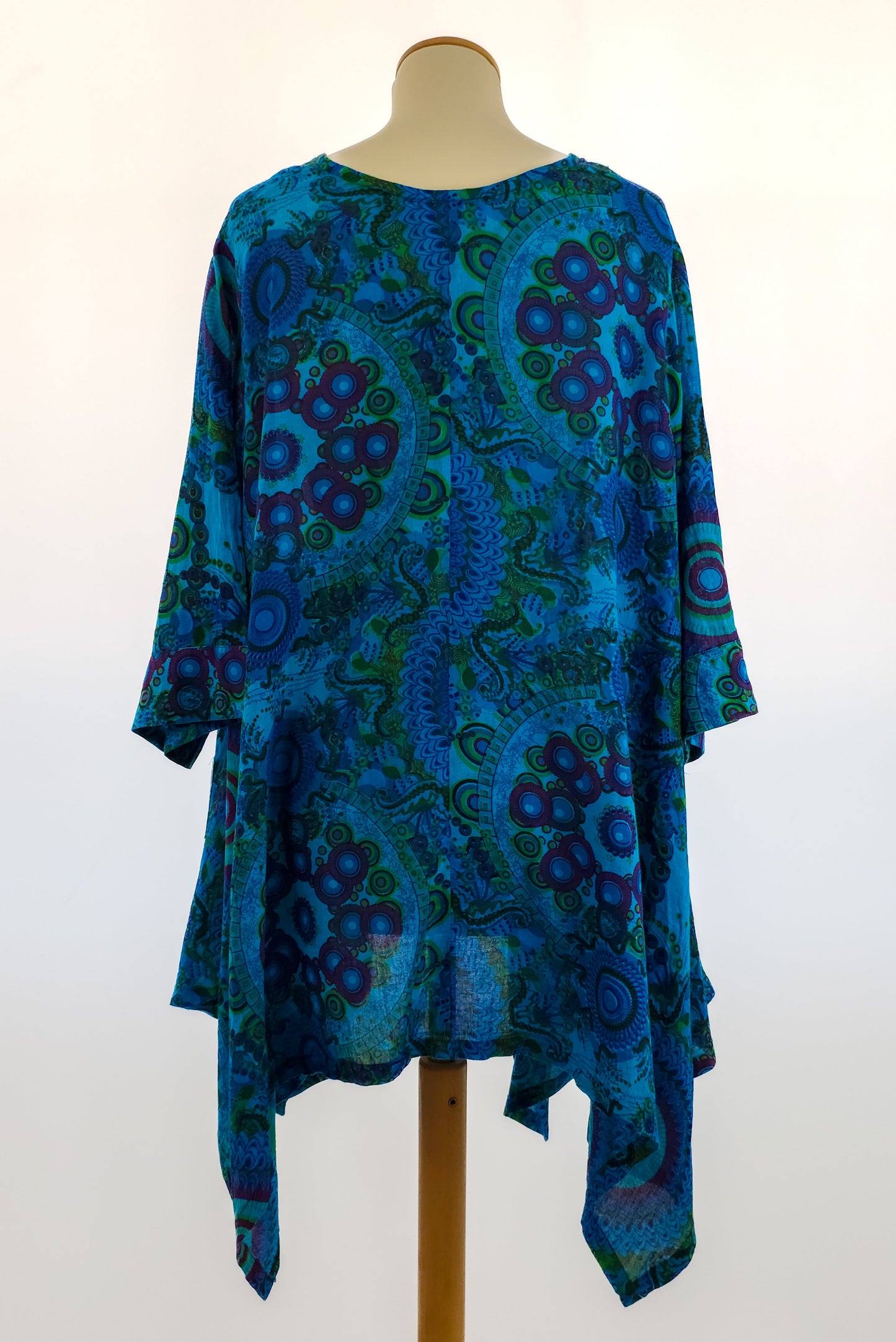 Blue and green bohemian tunic with vibrant circular and swirl patterns, three-quarter sleeves, and an asymmetrical hem, displayed on a mannequin.