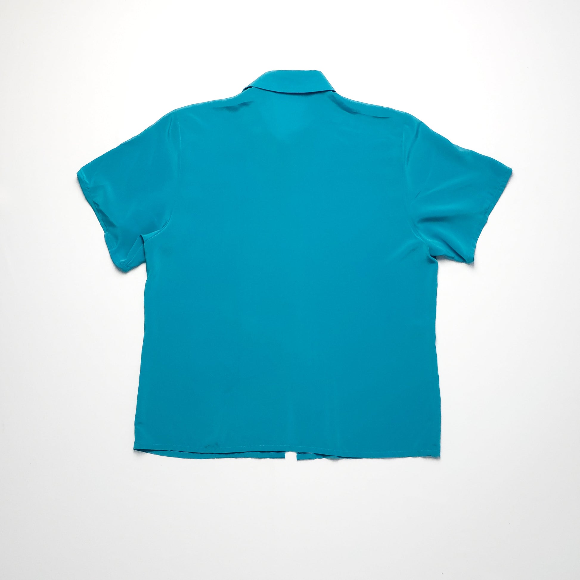 A teal short-sleeve shirt with a collar, laid flat on a white surface, viewed from the back. The shirt is plain with no visible patterns or buttons.
