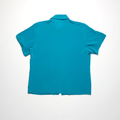 A teal short-sleeve shirt with a collar, laid flat on a white surface, viewed from the back. The shirt is plain with no visible patterns or buttons.