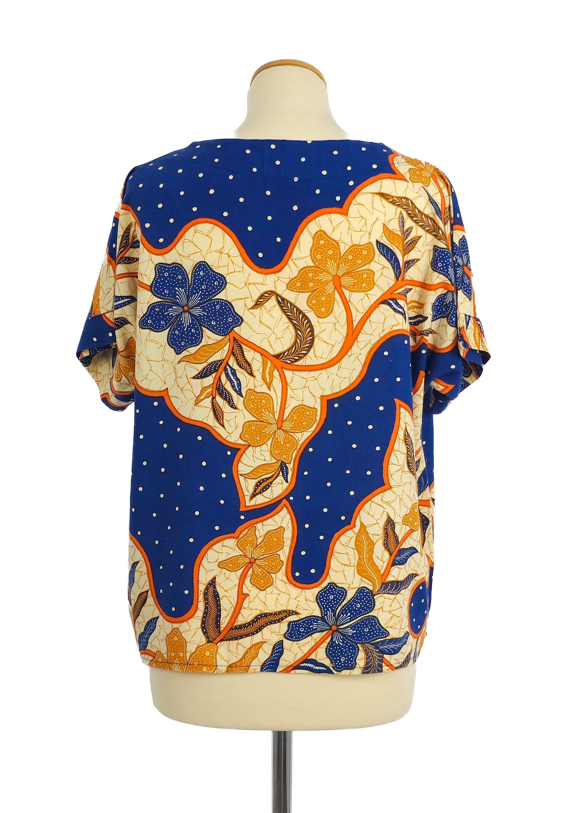 A short-sleeved top with a vibrant floral pattern featuring blue and orange flowers, set against a polka-dotted blue background, displayed on a mannequin.