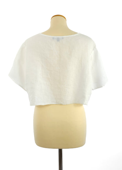 Back view of a white, short-sleeve, cropped linen top on a mannequin with a round neckline. The fabric has a loose, breathable texture.