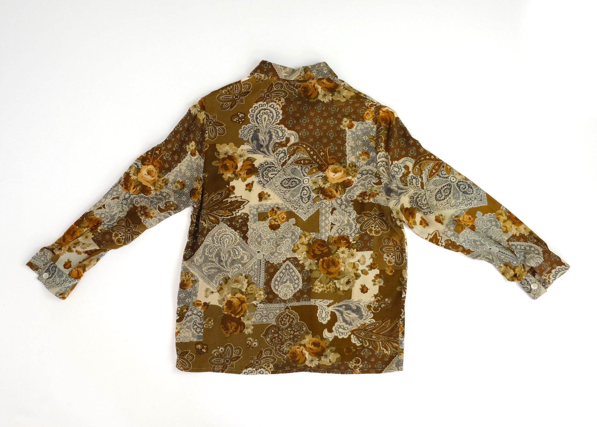 A vintage long-sleeve shirt with a brown, orange, and blue floral and paisley patchwork pattern, spread collar, and relaxed fit, displayed on a white background.