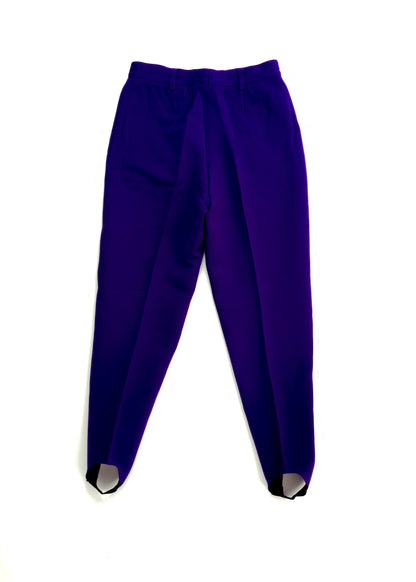 Bright purple stirrup pants with a pleated design, secured elastic foot straps at the ankles, and a high-waist fit, laid flat against a white background.