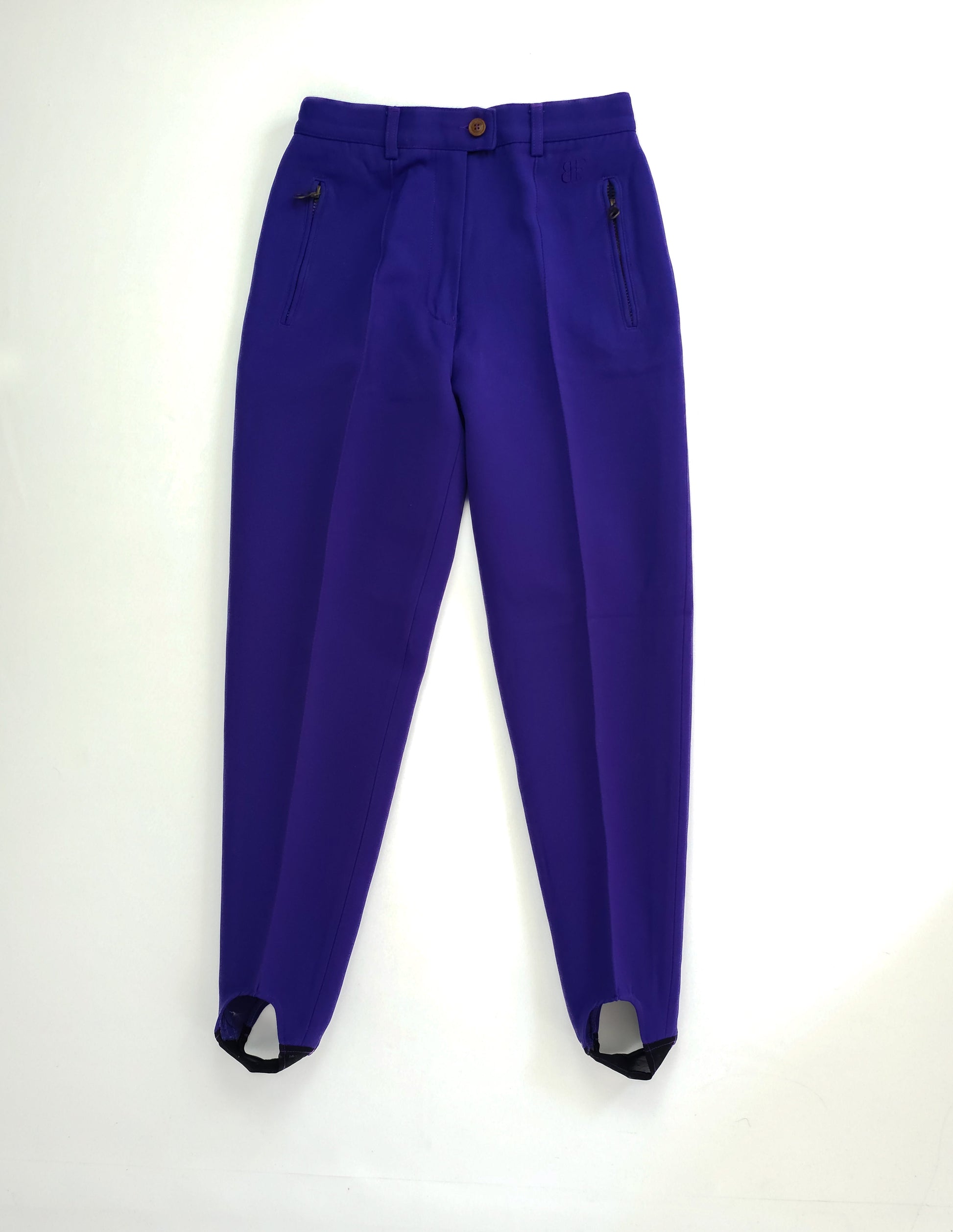 Indigo-colored stirrup leggings with a button closure and zippered pockets.