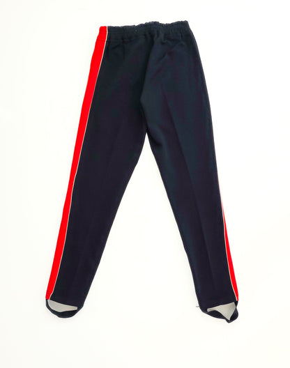 Black track pants with bright red side stripes, featuring a snug fit and stirrup foot straps, laid flat on a white background.